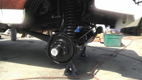 1989 Ford Bronco - The undercarriage of a vehicle is visible, supported by jack stands, with suspension and brake components exposed.