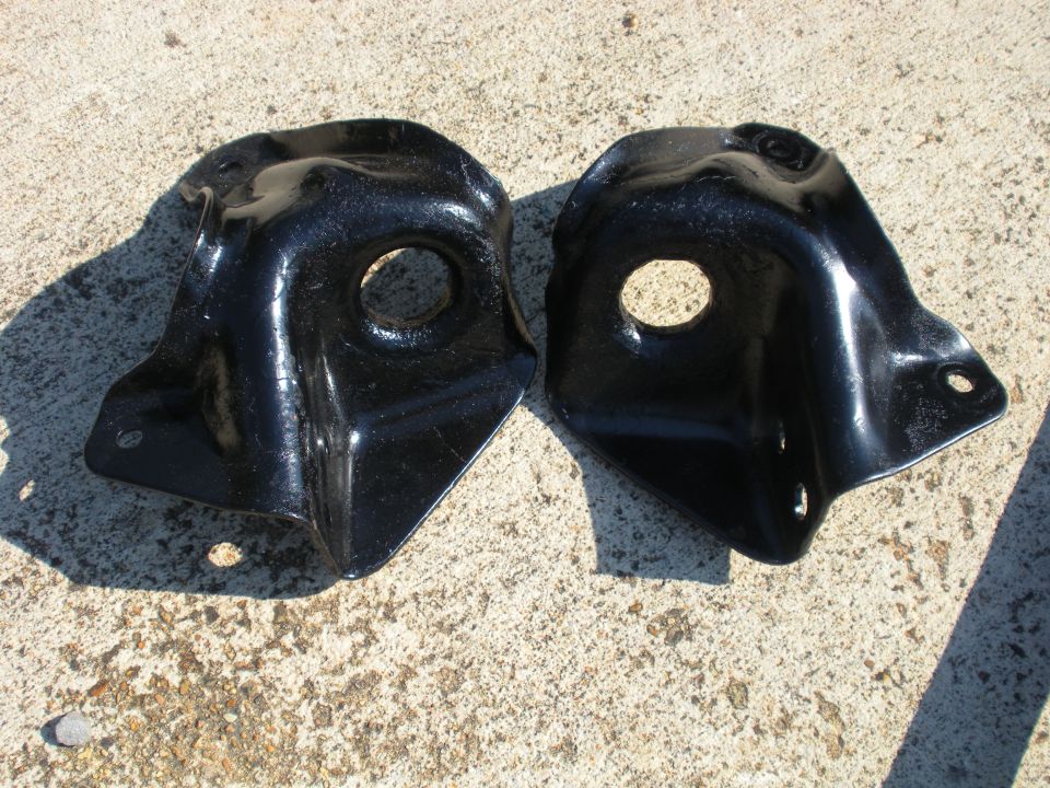 two black metal brackets with holes, sitting on concrete