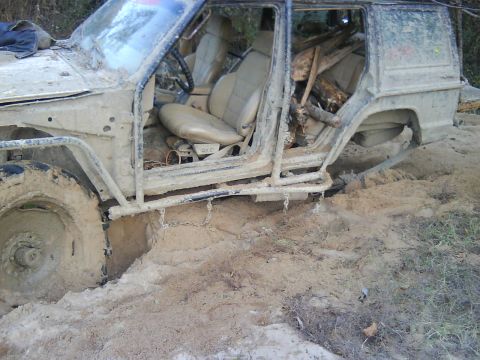 1978 Ford Bronco - This heavily modified off-road vehicle is stuck deep in the mud, with its doors removed and logs piled in the rear cargo area.