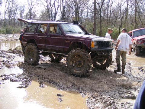 1978 Ford Bronco - Modified Jeep Cherokee XJ with large tires navigating a muddy off-road course.