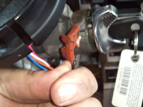 1994 Ford Bronco - A hand manipulates a red plastic connector with wires adjacent to a car's ignition cylinder and a key tag.