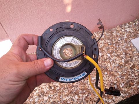 1994 Ford Bronco - A hand holds a vehicle clock spring part with visible wiring and a part number.