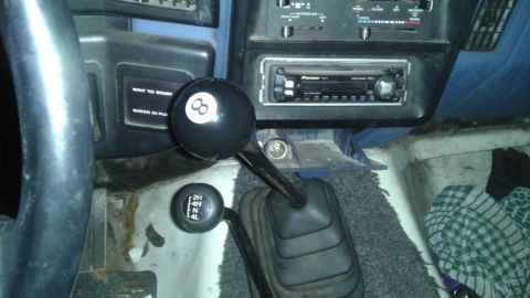 1989 Ford Bronco - The interior of a vehicle shows a manual transmission shifter and a transfer case shifter, along with an aftermarket stereo.