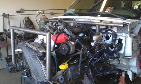 1992 Ford Ranger - The engine bay of a white truck is visible, showing a custom roll cage and exposed engine components.