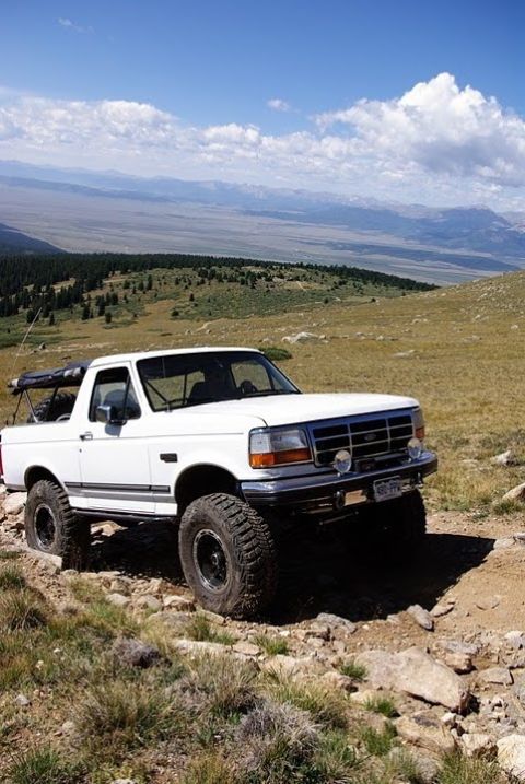 1995 Ford Bronco - White 1995 Ford Bronco navigates a mountain path under a blue sky.