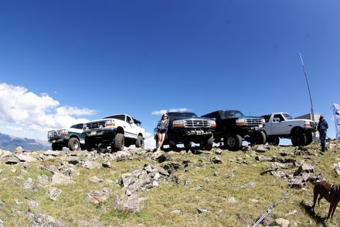 1995 Ford Bronco - A group of Ford trucks are parked on a mountain trail, with a clear blue sky overhead.