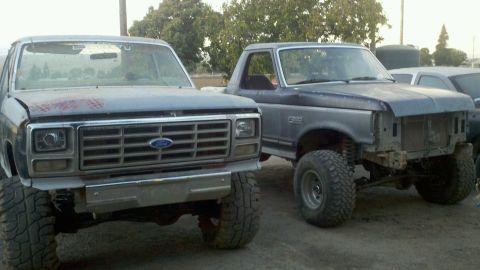 1989 Ford Bronco - Two Ford trucks are parked outdoors, one with a full front grille and the other missing its front end.