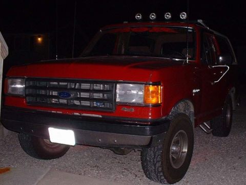 2006 Ford E350 - This red Ford Bronco features a distinctive grille and aftermarket roof lights, suggesting a model from the late 1980s.