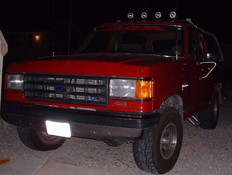 Red Ford Bronco with aftermarket lights on roof, front 3/4 view