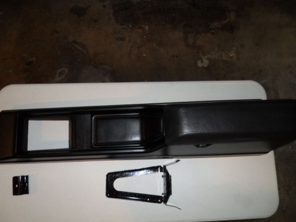 Black car interior console with two rectangular openings and a padded armrest, next to a metal bracket