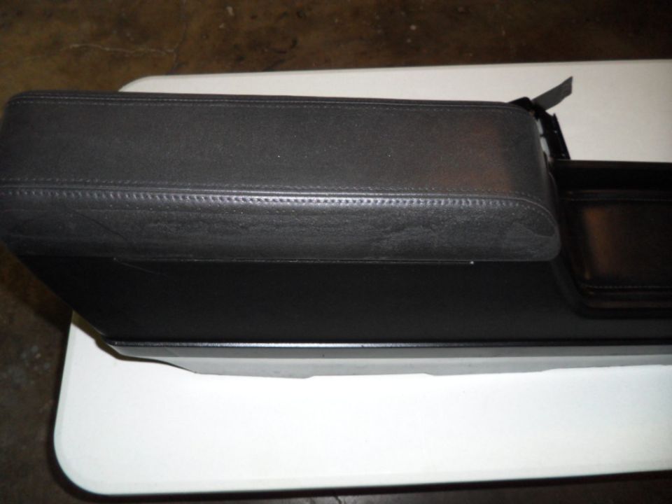Black leather car armrest with stitching and an open storage compartment next to it