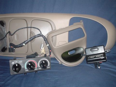 1999 Ford Taurus - Tan interior trim parts laid out on a blue cloth backdrop: an overhead console with map lights and a taped wiring pigtail, a dash instrumen…