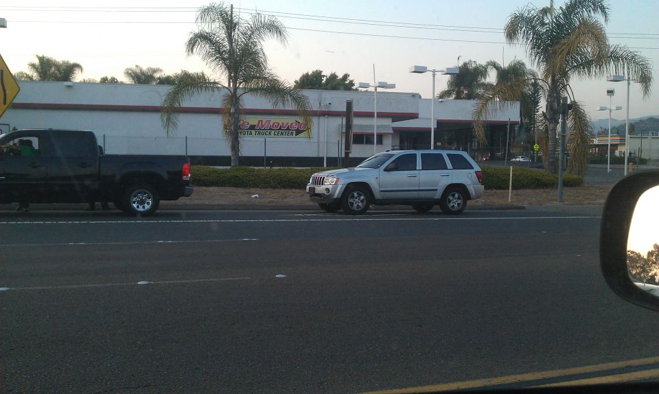 Silver Jeep Grand Cherokee parked next to a black pickup truck in front of a building with palm trees