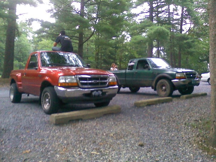 Red and green Ford Ranger pickup trucks parked side-by-side in a gravel lot