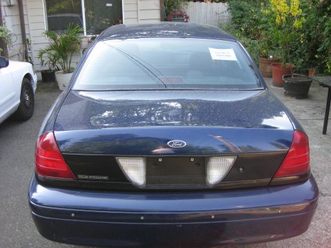 2003 Ford Crown Victoria - The rear of a Ford Crown Victoria Police Interceptor is shown, with a white vehicle partially visible to the left.