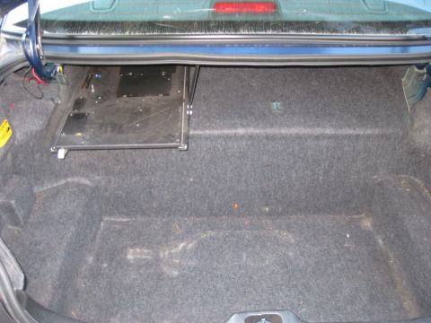 2003 Ford Crown Victoria - The interior of a car's trunk shows a carpeted floor and a metal component installed on the right side.