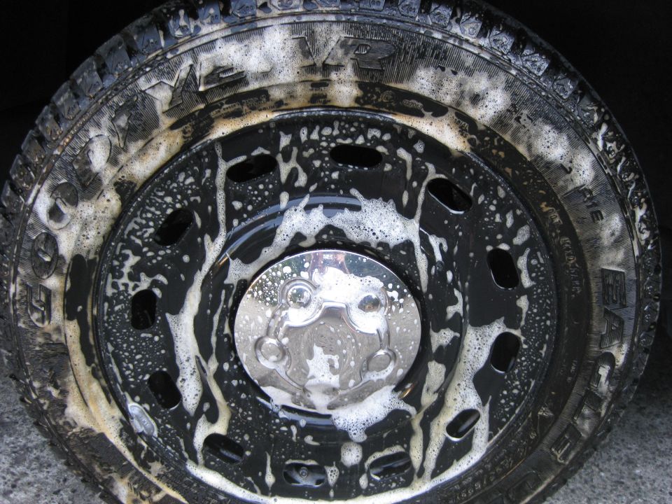 Close-up of a soapy truck wheel and tire with a chrome hubcap