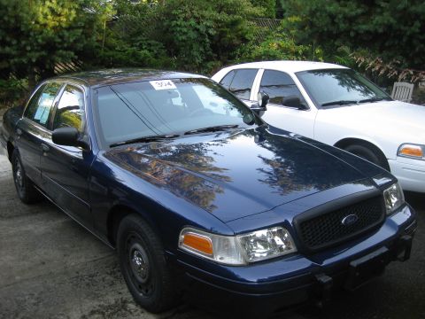 2003 Ford Crown Victoria - Two Ford Crown Victorias, one dark blue and one white, are parked outdoors.