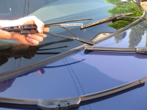 2003 Ford Crown Victoria - A hand holds a windshield wiper over the hood of a blue car, with several other wipers visible.