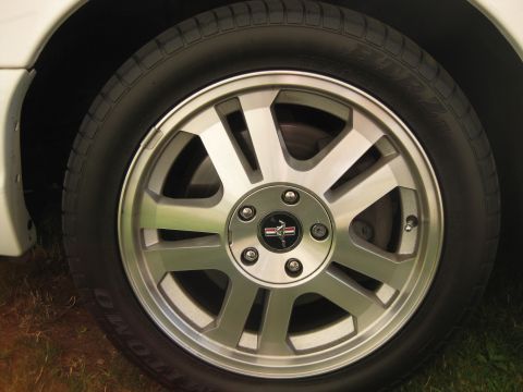 2003 Ford Crown Victoria - Close-up of a car's wheel, showing a silver alloy rim with a Mustang emblem and tire.