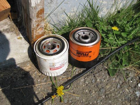 2003 Ford Crown Victoria - Two oil filters, a white Motorcraft and an orange FRAM, are placed on the ground outdoors.