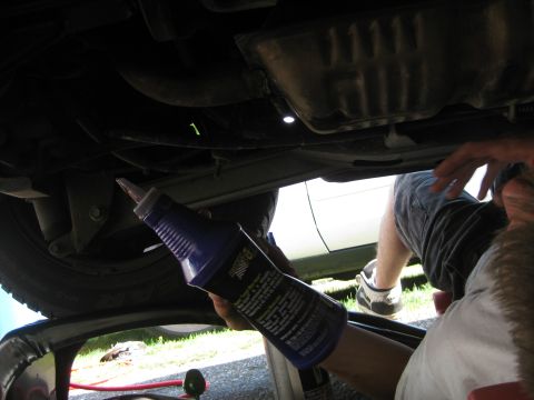 2003 Ford Crown Victoria - Underneath view of a car during an oil change with a hand holding an oil additive bottle.
