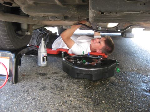 2003 Ford Crown Victoria - A person performs maintenance under a vehicle, with tools and supplies nearby.