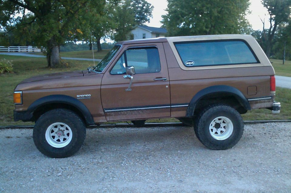 Brown 1987 Ford Bronco with a tan removable top, side view, lifted suspension, white rims