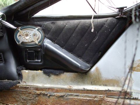 2000 Ford E350 - Close-up of a car's interior door panel, showing a speaker and armrest, with significant rust on the lower body.