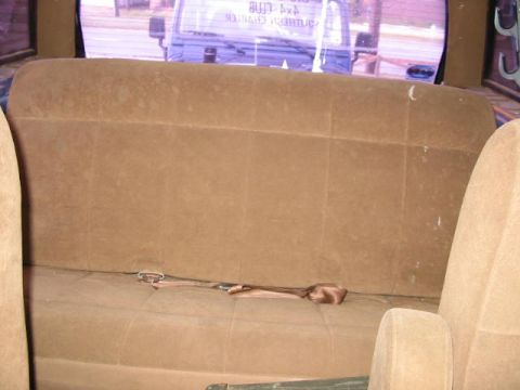 1986 Ford Bronco - The interior of a vehicle shows a brown bench seat and a view of another vehicle through the rear window.