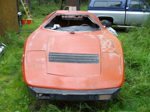 2000 Ford E350 - This orange sports car is in a state of disrepair, with a missing windshield and visible wear. It is parked outdoors next to a pickup truck.