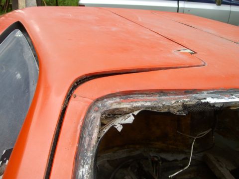 2000 Ford E350 - The orange paint on this vehicle's roof is faded, and the window frame is heavily damaged and rusted.