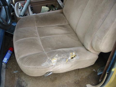 1986 Ford Bronco - The interior of a vehicle shows a worn-out tan seat with visible damage and a spray can on the floor.