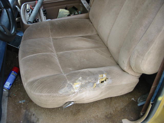 Worn tan cloth bench seat with torn cushion exposing foam padding