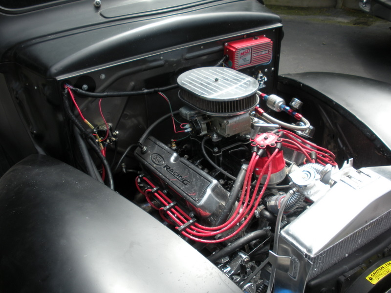 Engine bay showing V8 engine with MSD ignition box, Holley carburetor, and red spark plug wires. "Ford Racing" is visible on valve cover