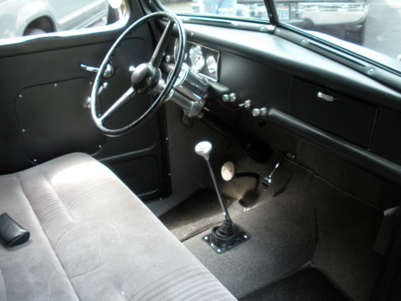 Interior view of a vintage truck cab, showing the steering wheel, dashboard, bench seat, and floor shifter