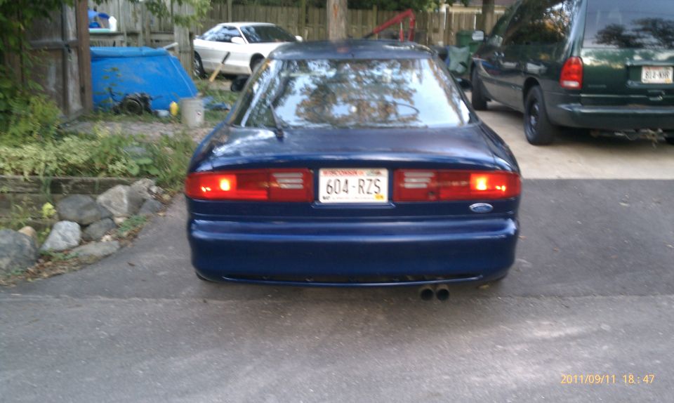 Blue Ford Probe rear view with license plate 604-RZS. A white car and a green van are visible in the background