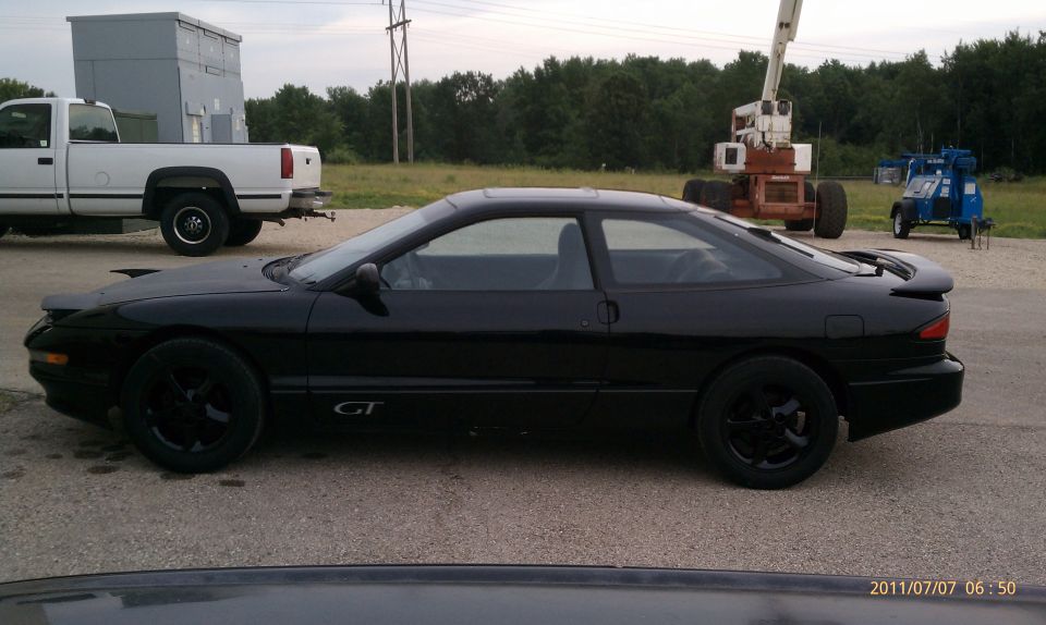 Black Ford Probe GT coupe, driver-side view, black wheels, parked on gravel lot