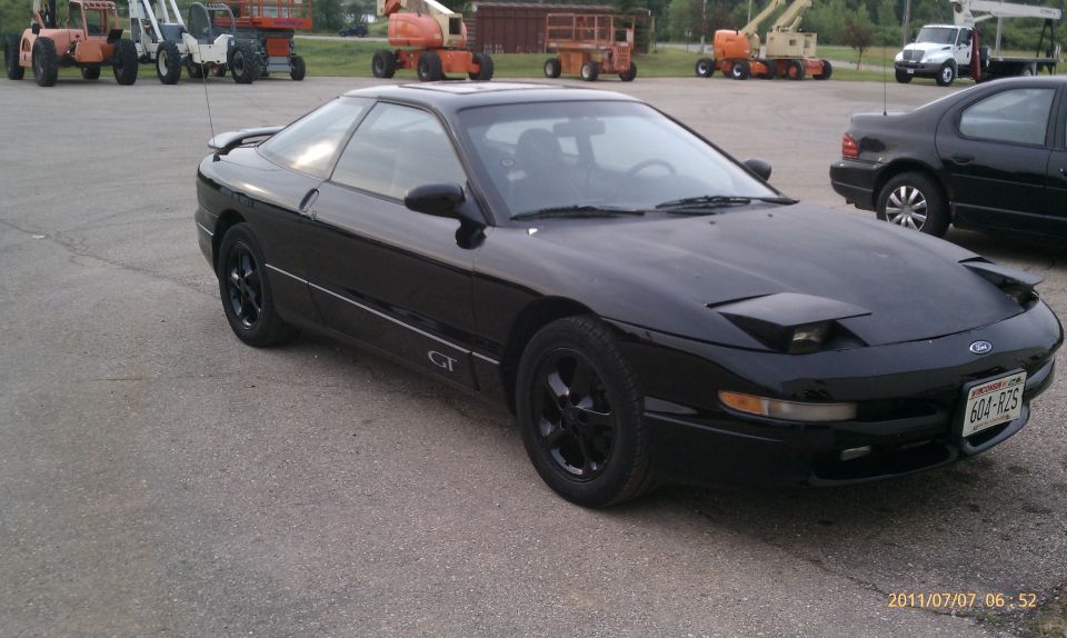 Black 1994 Ford Probe GT parked in a lot with construction equipment and another car behind it