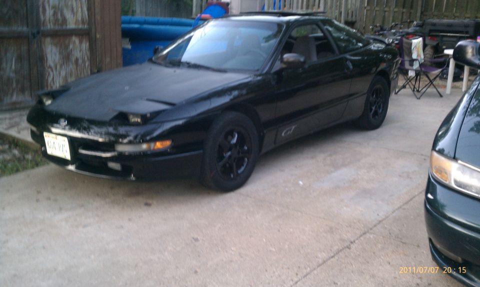 Black coupe with pop-up headlights and 'GT' badging on the side, parked on concrete