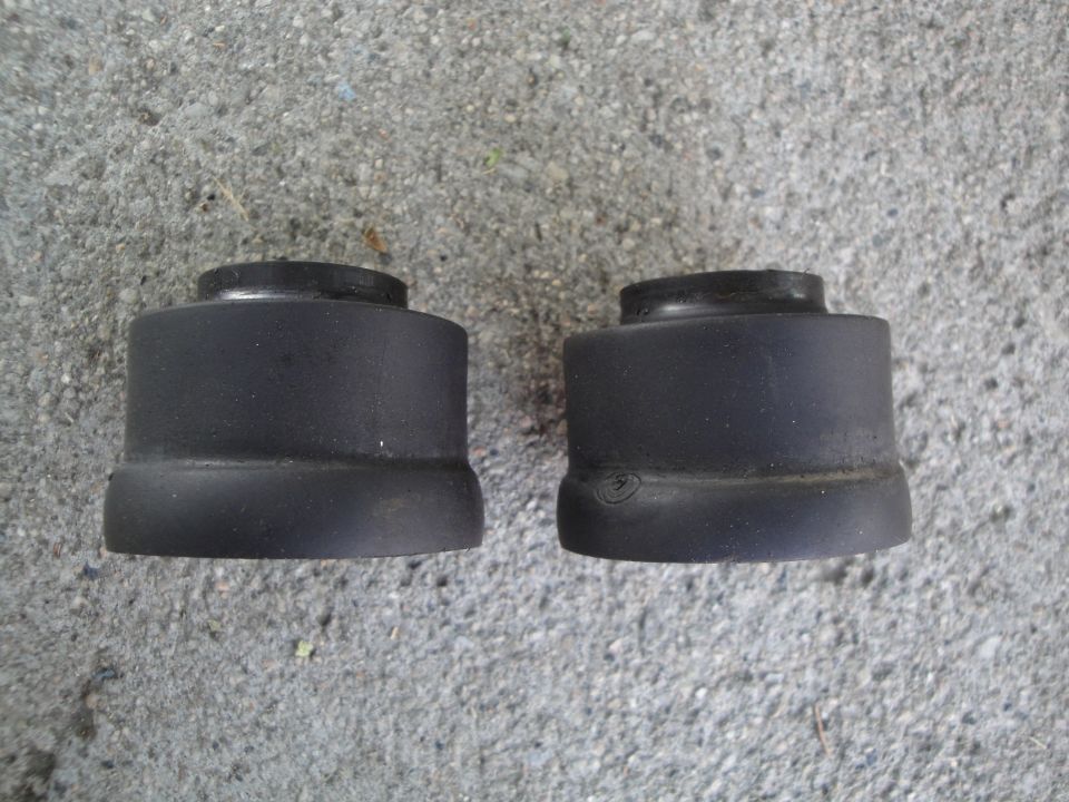 two black rubber suspension bushings sitting on concrete