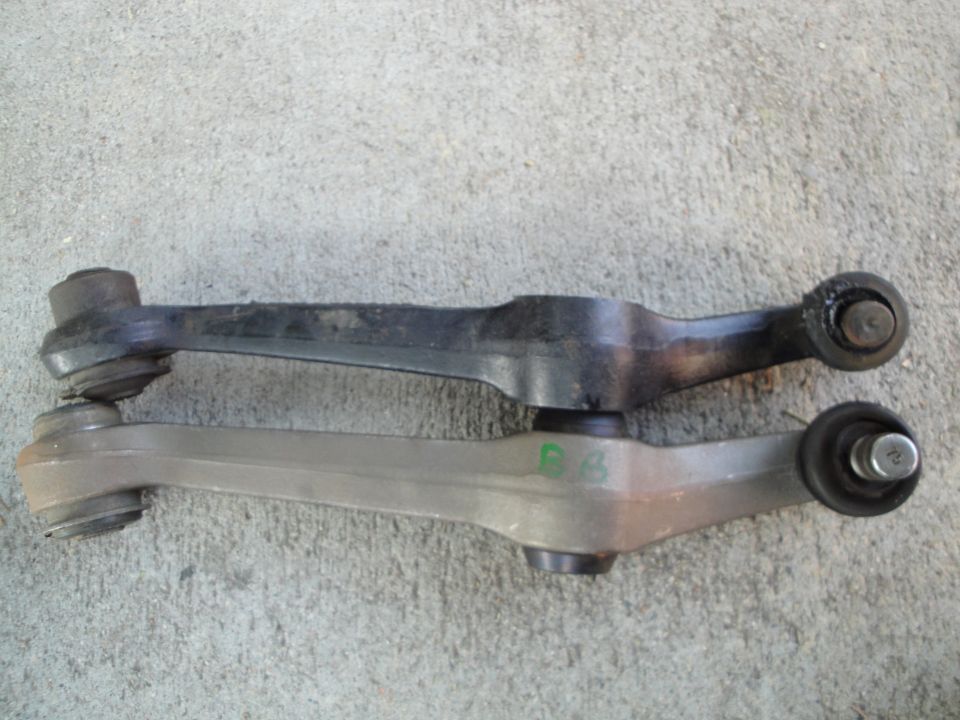 Two automotive control arms, one black and one silver, with green markings on the silver one
