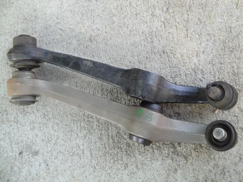 1995 Ford Taurus - Comparison of two automotive control arms, one black and one silver, against a concrete background.