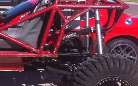 Suzuki Samurai - Close-up view of the suspension and large tire of a custom red off-road buggy, with a red car visible behind it.