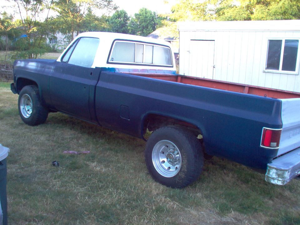Pickup truck, dark blue body, white cab, parked on grass next to a white building