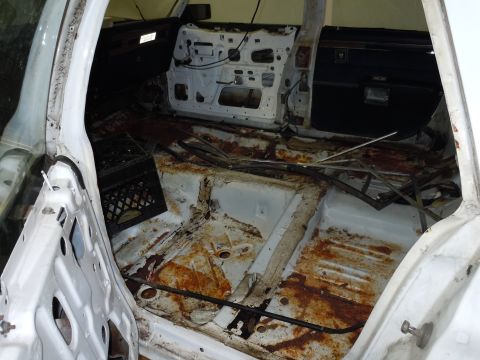 2001 Ford Crown Victoria - The interior of a car is shown with significant rust on the floor and the door panels removed, indicating extensive disrepair.