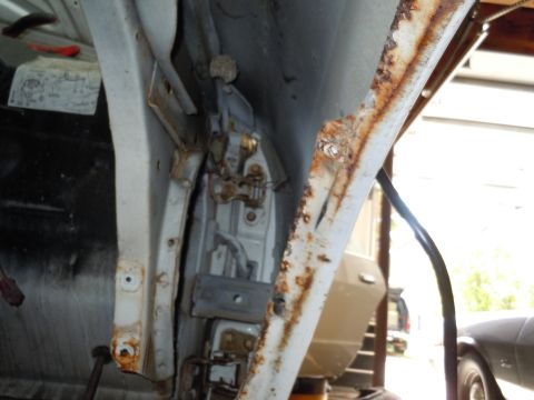 2001 Ford Crown Victoria - Close-up view of a heavily rusted car door hinge area, showing the latch mechanism.