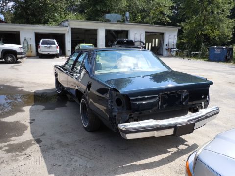 2001 Ford Crown Victoria - This dark green 2001 Ford Crown Victoria is seen from the rear, with its quarter panels and bumper removed, parked outside a garage.