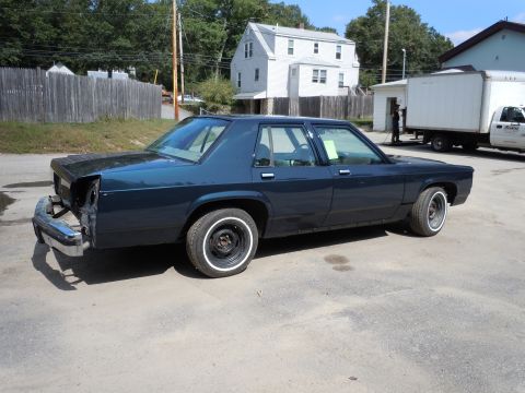 2001 Ford Crown Victoria - Sedan with missing rear bumper and headlights, parked in an outdoor lot with buildings in the background.