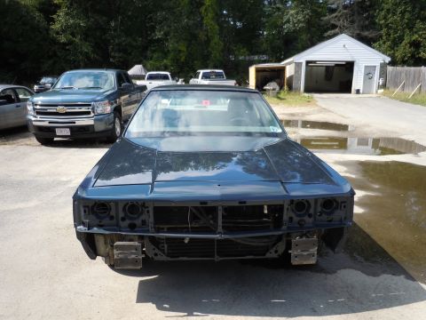 2001 Ford Crown Victoria - A dark sedan sits in a driveway, its front end disassembled, with a pickup truck parked nearby.